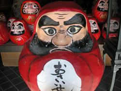Japanese daruma doll with red body, characters in black on white belly, black bushy beard and eyebrows